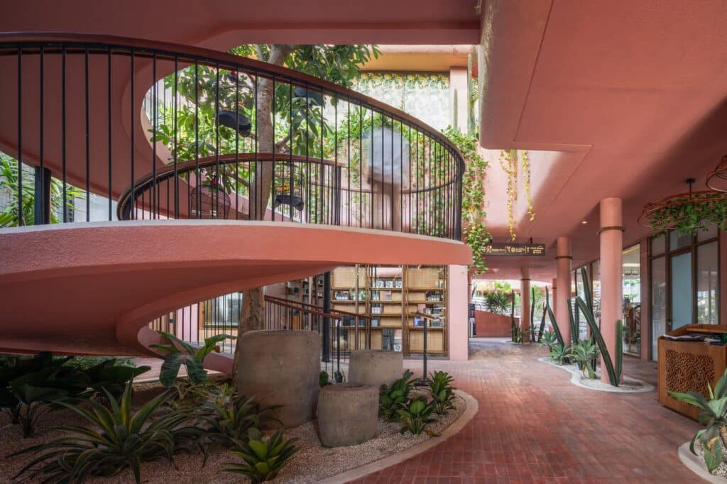 Interior circulation space at The LUC Lifestyle featuring a pink spiral staircase, indoor plants, and boutique storefronts.
