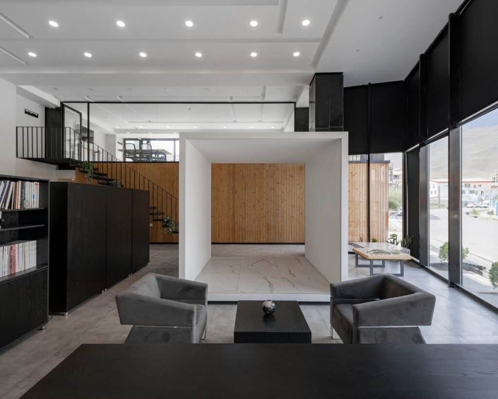 Interior view of Ramand Ho office featuring a central white cube, grey armchairs, and minimalist wooden walls.
