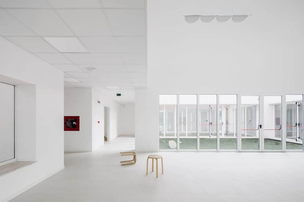 Minimalist white interior corridor with large glass windows overlooking a central courtyard.