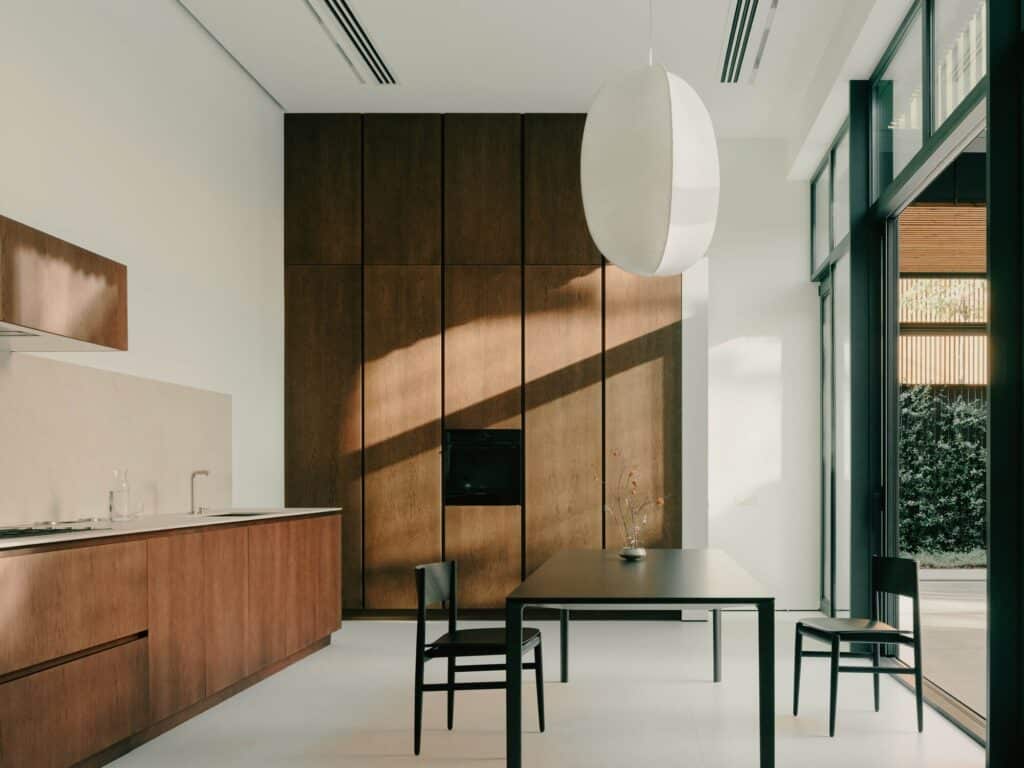 Modern minimalist kitchen interior in the Okrokana house featuring warm natural wood cabinets and a large oval pendant lamp.