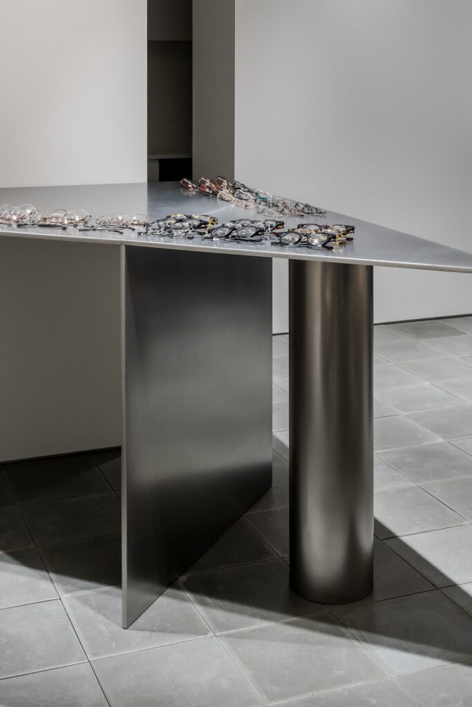 Close-up of a minimalist metal triangular display table with eyewear collections in Ashiya Optical Store.