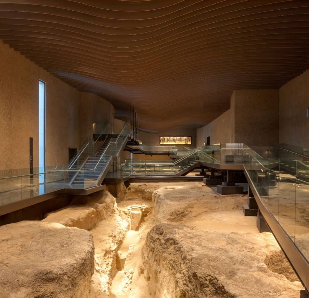 Interior of Al Ain Museum showing an in-situ archaeological excavation site with elevated glass walkways and a wave-like ceiling.