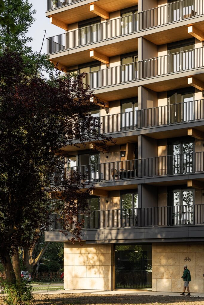 Close-up of the CLT timber beams and balcony structure of Valckensteyn, with lush green trees in the foreground.