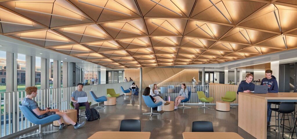 Students studying in a modern lounge area under a geometric wooden ceiling at the ECoRE building.