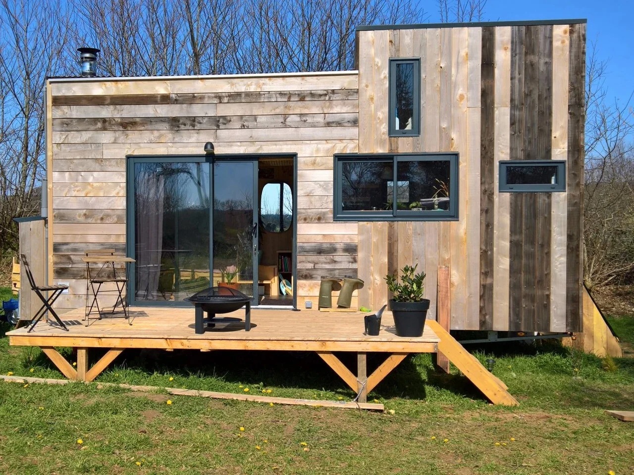 Exterior view of the Chillhouse, a sustainable tiny home featuring natural wood cladding and an elevated wooden deck under a clear blue sky.