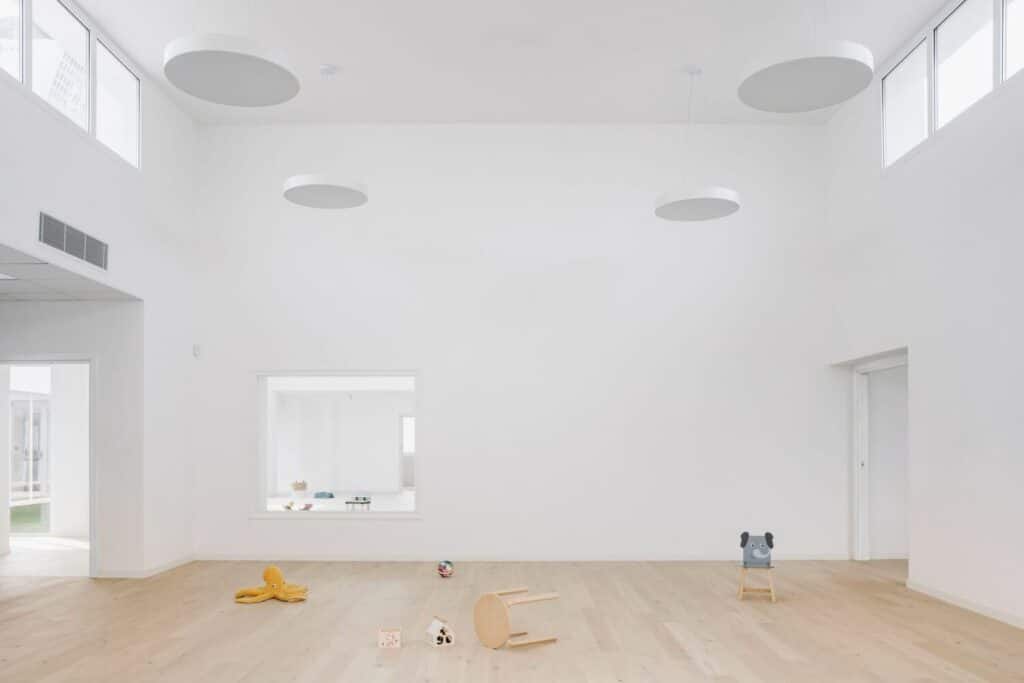 Spacious nursery activity room with oak wood flooring and circular pendant lights.