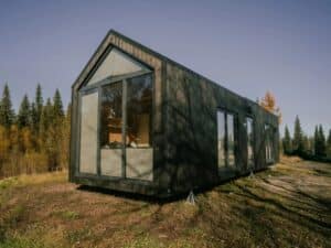 Exterior of Zenith tiny house featuring dark wood cladding, large floor-to-ceiling windows, and a modern gabled roof design.