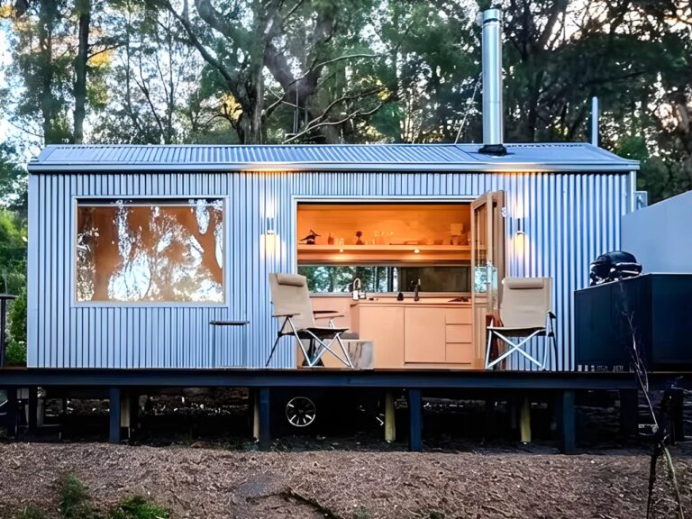 Exterior view of a modern prefabricated cabin with corrugated metal zinc cladding and a warm wooden interior visible through open doors.