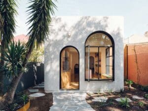 Modern white textured extension of an Adelaide cottage featuring large black-framed arched windows and a stone pathway.