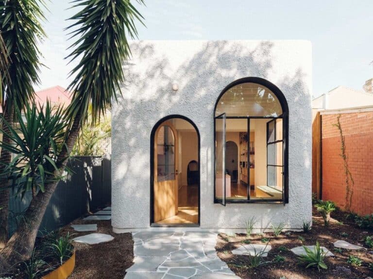 Modern white textured extension of an Adelaide cottage featuring large black-framed arched windows and a stone pathway.