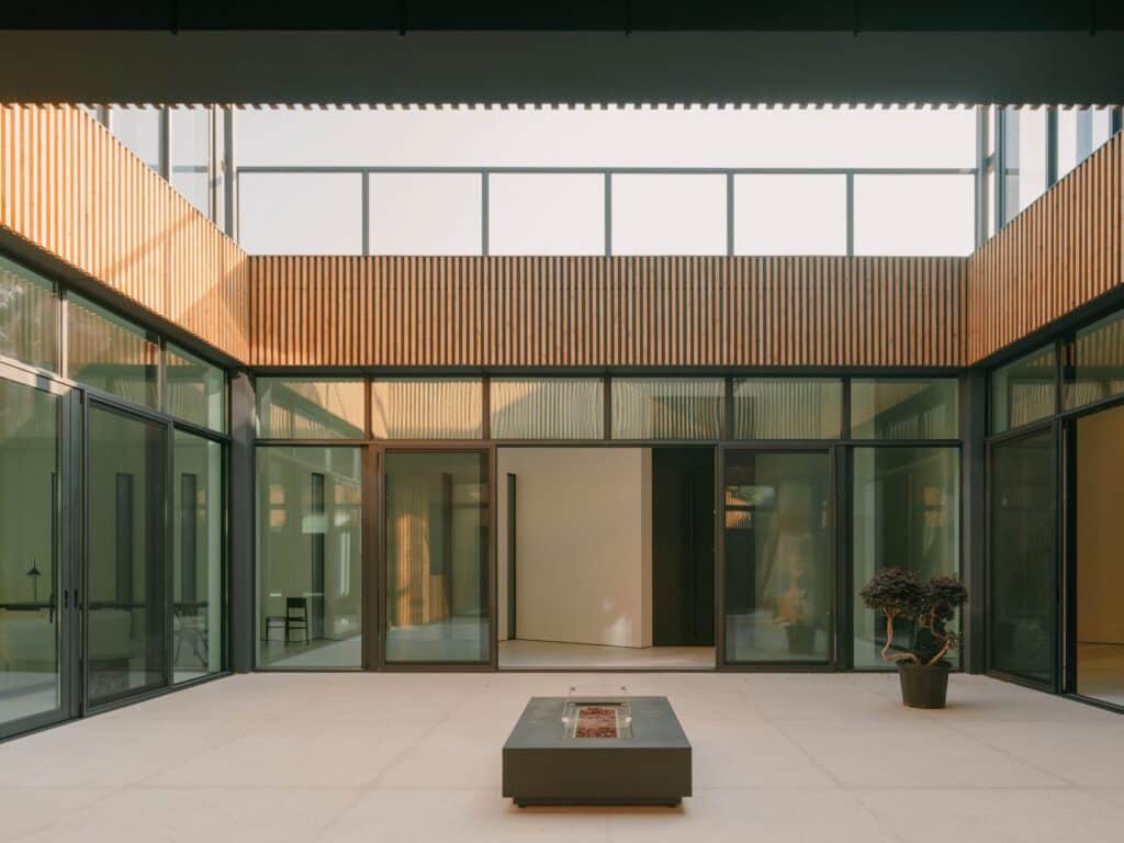 Spacious central courtyard of the Okrokana residence with glass walls and vertical wooden slat cladding.