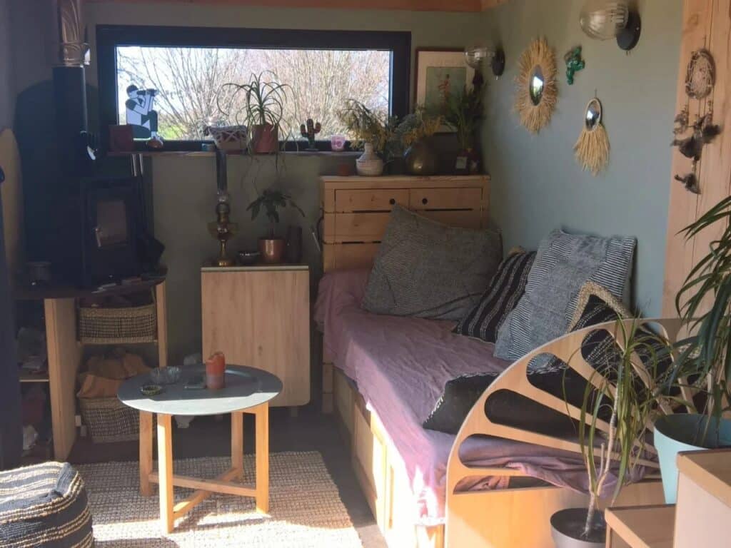 Cozy interior of the Chillhouse living area with a low-profile sofa, wooden furniture, a wood-burning stove, and natural light from a horizontal window.