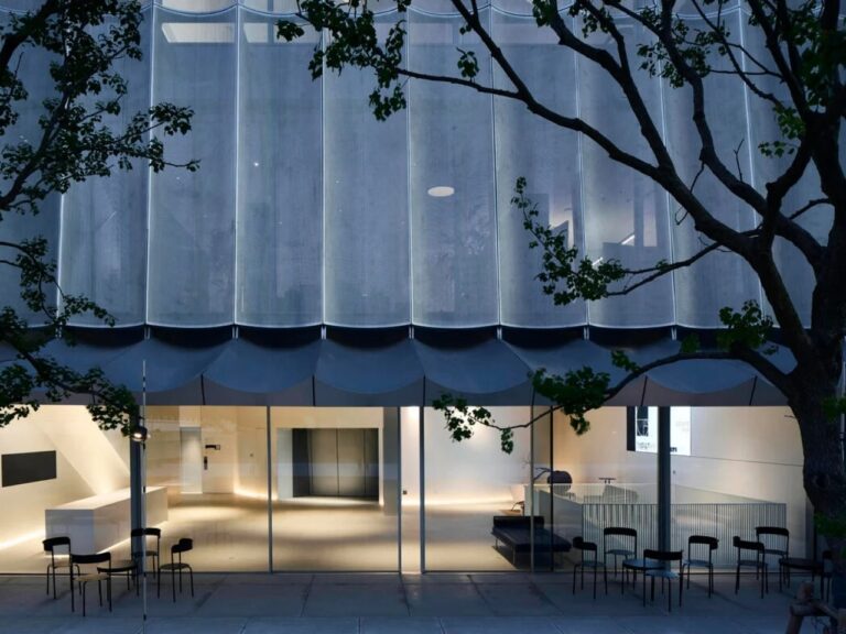 Interior view of Hangzhou Empathy Museum reception area at dusk with glass facade and minimalist black chairs.