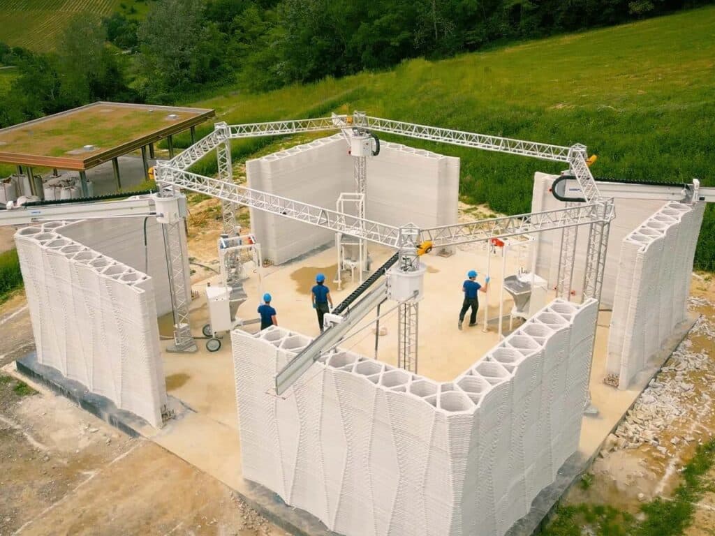 Aerial view of the sustainable 3D-printed farm project in Northern Italy, showing robotic arms on a hexagonal structure building dual-dome walls.