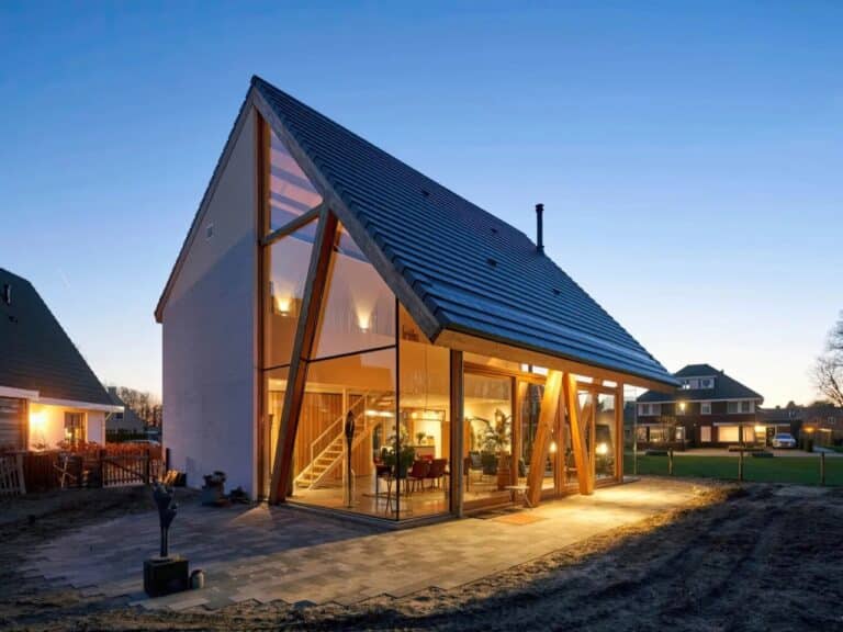 Exterior evening view of a modern catalog barnhouse in the Netherlands featuring a prominent gabled roof and glowing glass facades.