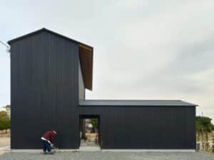 Minimalist dark charred wood facade of Onomichi House by Studio Bark in Japan, featuring Yakisugi cladding and a central sheltered entrance.