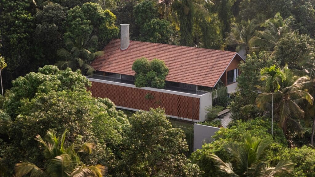 Aerial view of Haven House nestled within a dense tropical forest, showing its sloped red tile roof.