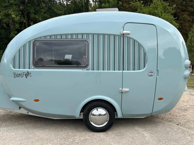 Side view of the light blue Barefoot Bothy fiberglass travel trailer with a retro rounded design and striped window graphics.