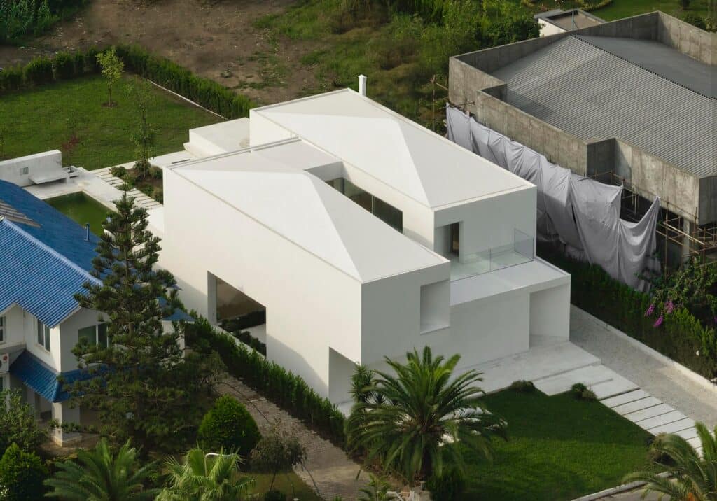 Aerial view of a white contemporary villa with a unique roof design, situated within a residential neighborhood.