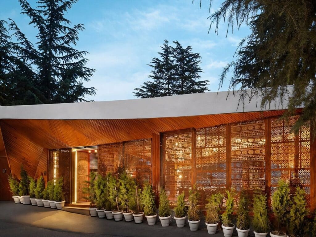 Entrance of Ayla project with intricate wooden latticework and local stone walls illuminated at dusk.