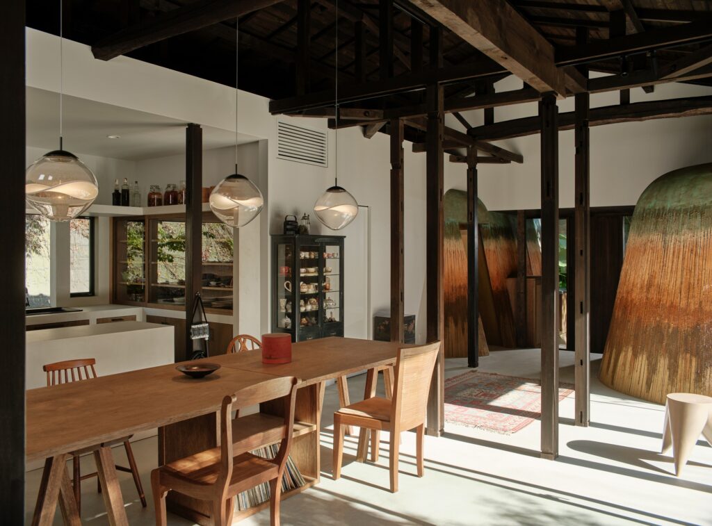 Modern dining area in Haniyasu House with wooden furniture, glass pendant lights, and earth-textured structural additions in the background.