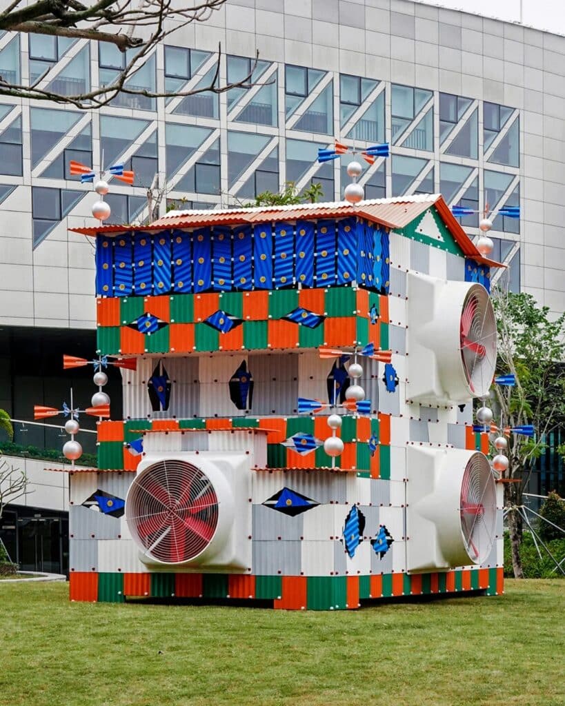 A wide perspective of the Clock House No. 2 pavilion situated on a green lawn with a modern glass building in the background.
