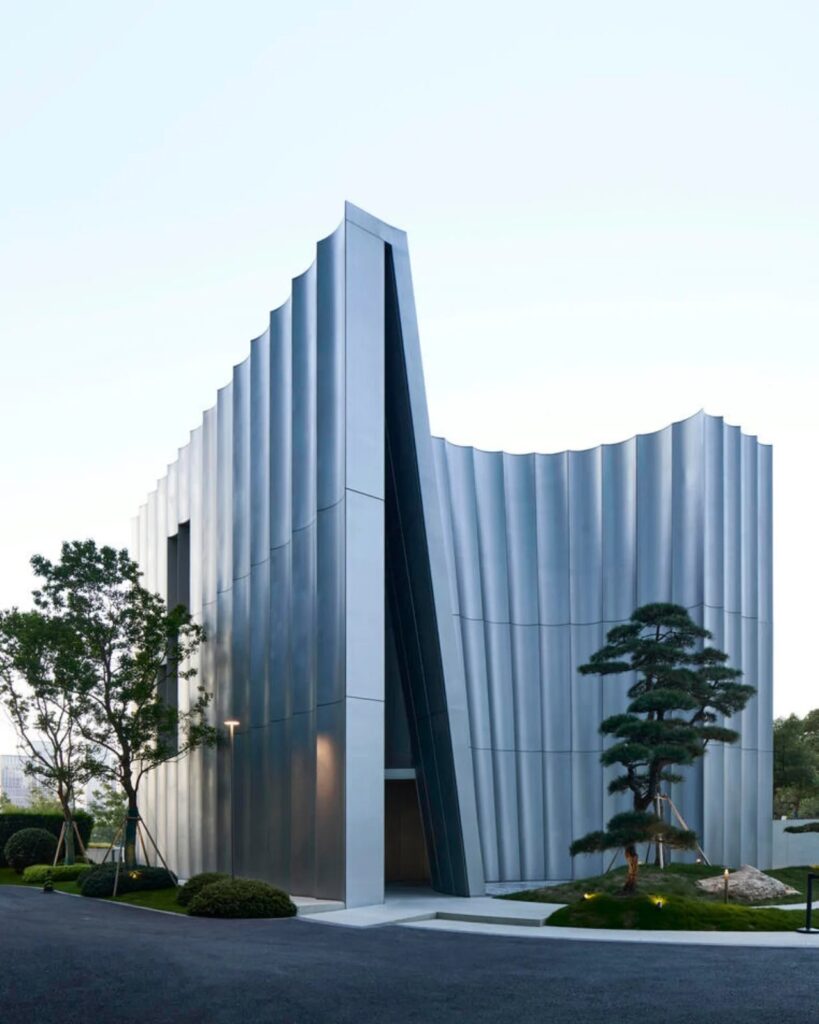 Exterior view of Hangzhou Empathy Museum featuring curved stainless steel facade and sculptural pine tree.