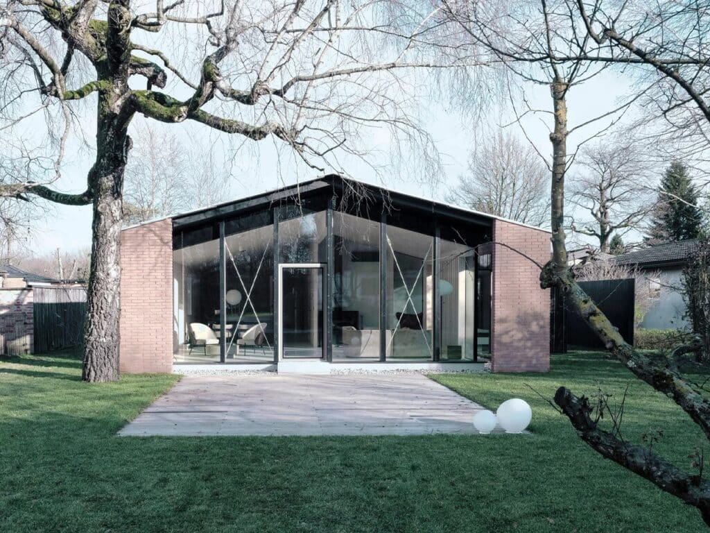 Symmetrical view of a modern house gable end with floor-to-ceiling glass windows and a green lawn.