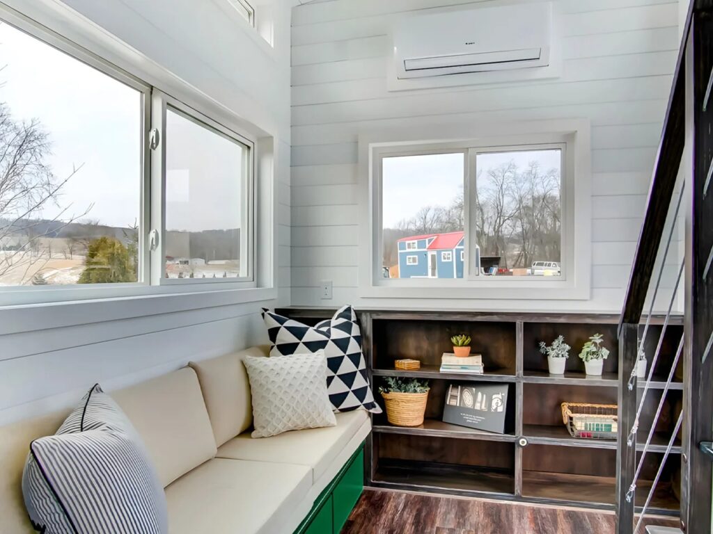 Bright interior of Kinnakeet house living area with a cream sofa, built-in dark wood bookshelves, and large windows for natural light.