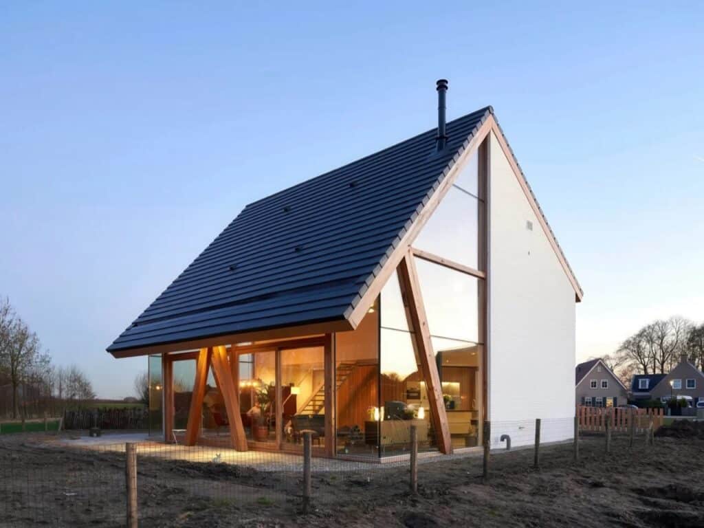 Night view of a modern house on a triangular plot in Werkhoven with visible timber support columns and floor-to-ceiling glass walls.