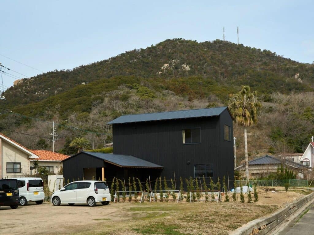 Exterior view of Onomichi House by Studio Bark set against a lush mountain backdrop in Japan, showing two connected structures.