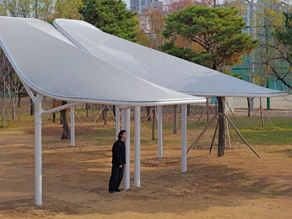 A person standing next to a Seoul Wing support column, providing a sense of the canopy's height and scale.