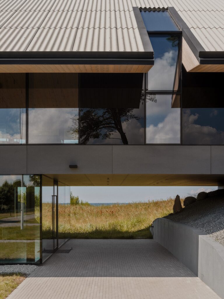 Close-up of the building's elevated structure showing a sheltered walkway underneath and a view of the sea in the distance.