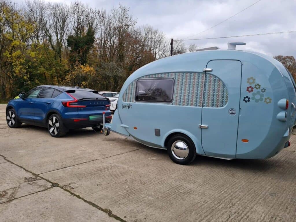 A blue Volvo electric SUV towing a Barefoot Bothy micro-caravan on a paved surface.