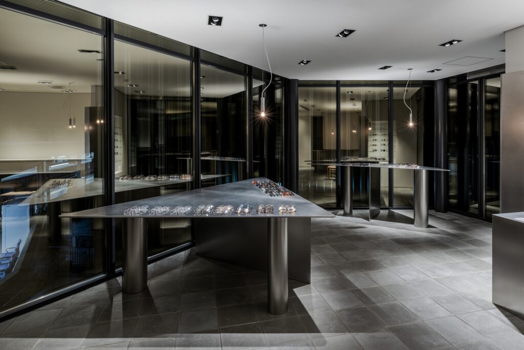 Night view of Ashiya Optical Store interior with focused pendant lighting over triangular eyewear displays.