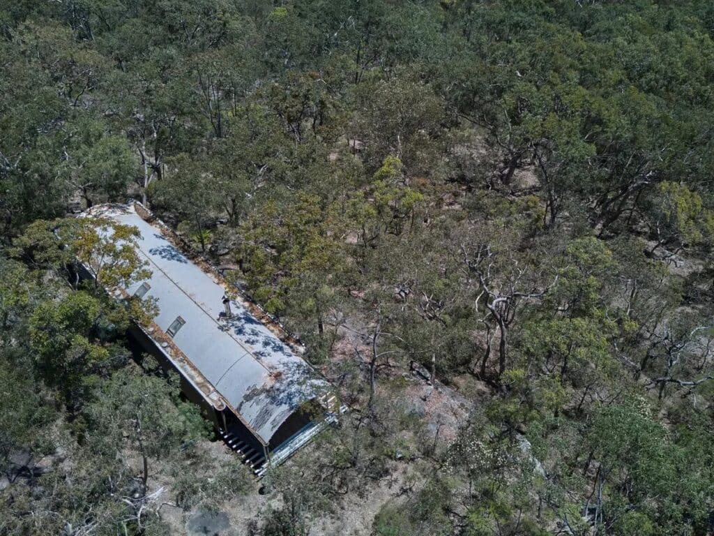 Aerial bird's-eye view of the Ball-Eastaway House long corrugated roof hidden within a dense Australian forest.