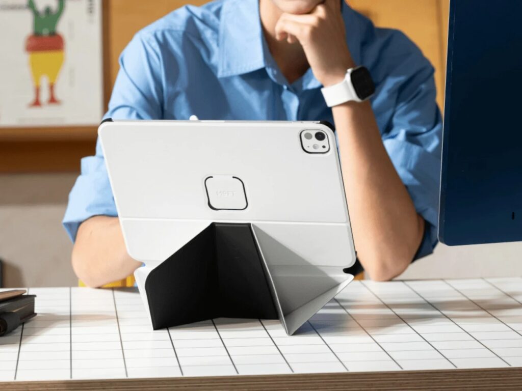 Rear view of a white iPad in a MOFT folio case with an origami-inspired black stand being used by a person at a desk.