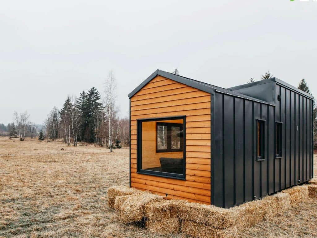 Side angle of Tiny Hogwarts featuring black corrugated metal cladding and a large picture window reflecting the outdoor scenery.