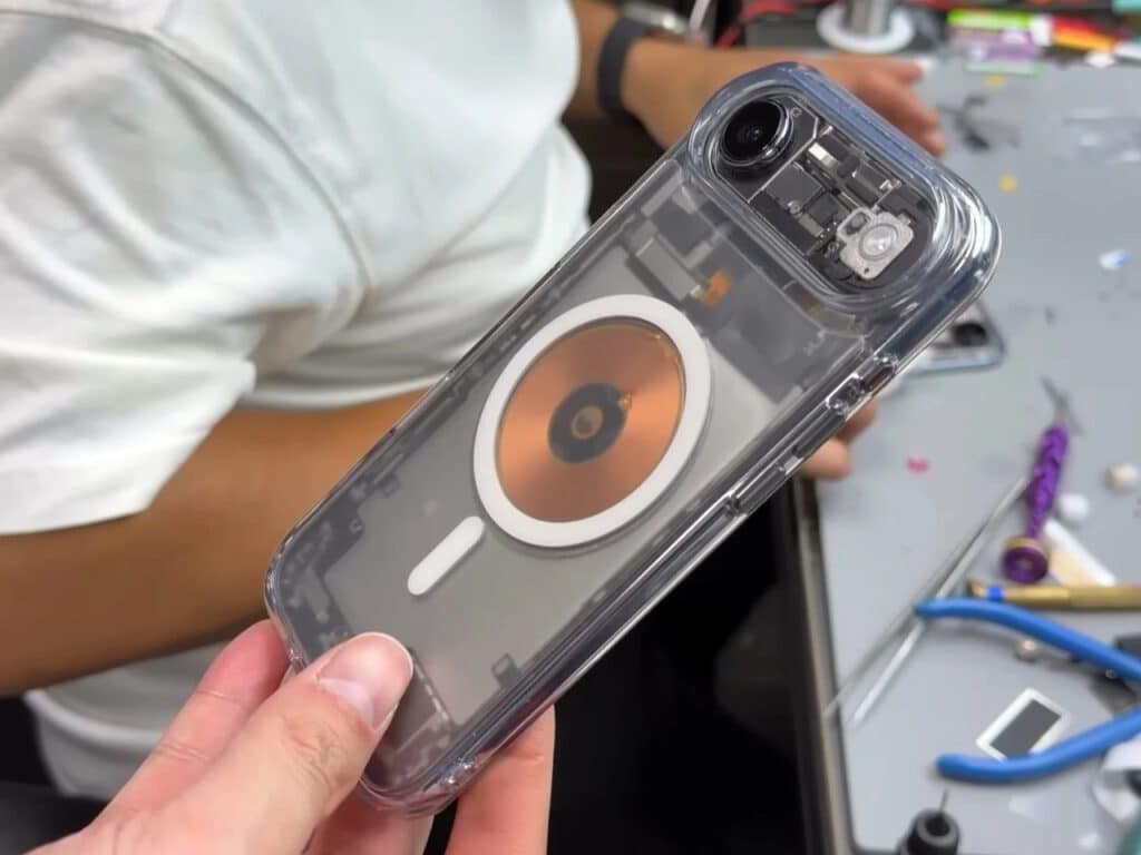 Close-up of a modified iPhone with a MagSafe ring and copper coil visible through a clear back panel.