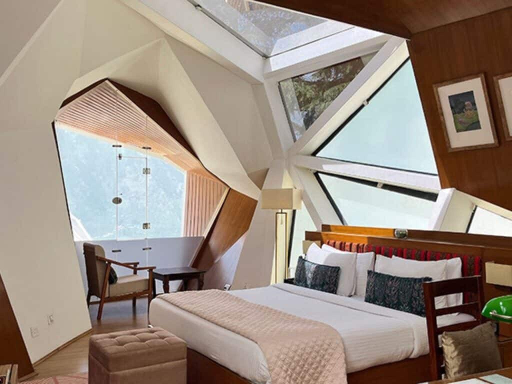 Interior of a luxury bedroom inside a biomorphic pod with a large geometric skylight and mountain views.