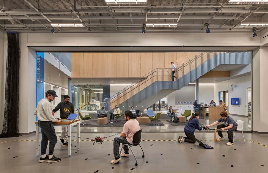 Students testing drones in an indoor flight lab behind a glass partition at the ECoRE building.