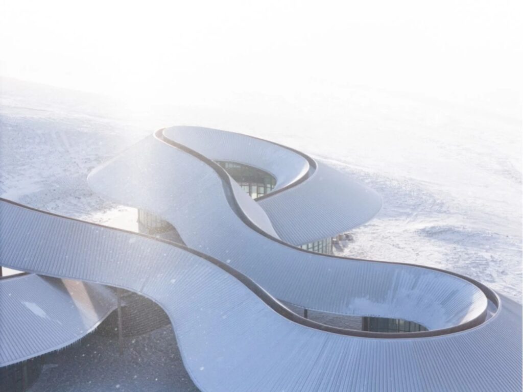 Close-up of the winding 274-meter walkway roof at the Volcano Visitor Center, covered in snow with sunlight reflecting off the metal panels.