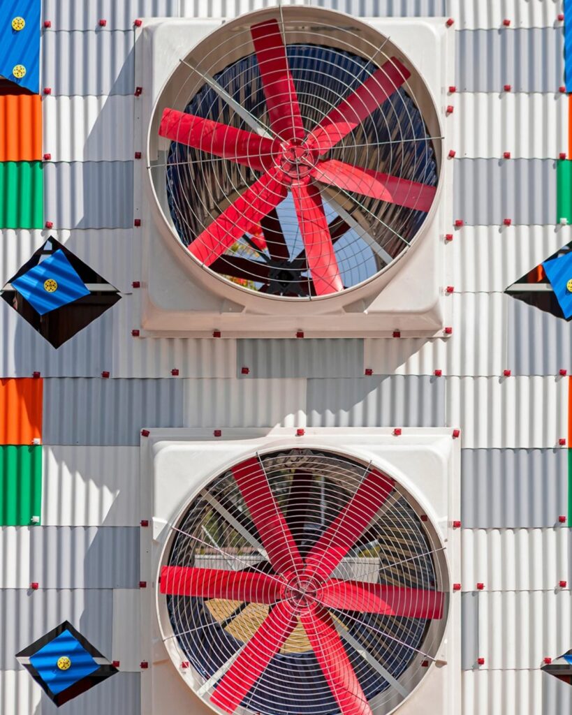 Close-up of two large white industrial fans with red blades mounted on a gray and white corrugated wall of Clock House No. 2.