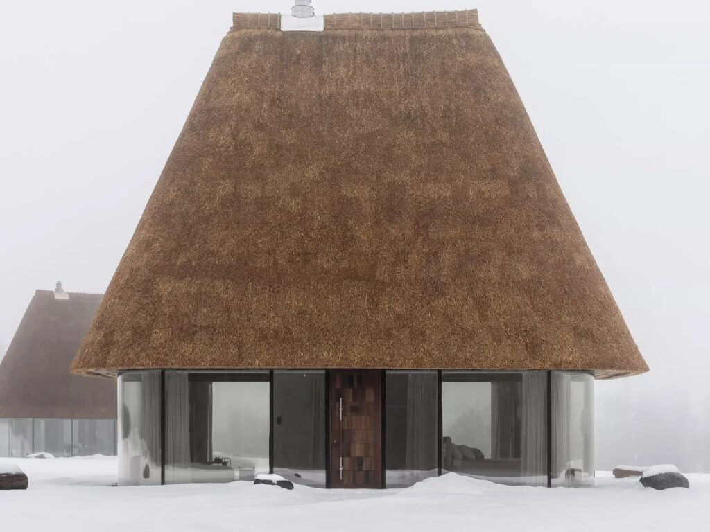 Symmetrical view of a modern guesthouse with a dark wooden door centered between glass panels under a large thatched roof.