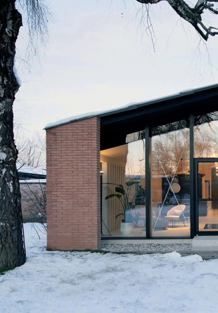 Close-up of a brick wall and glass window reflecting the sunset with indoor plants visible.