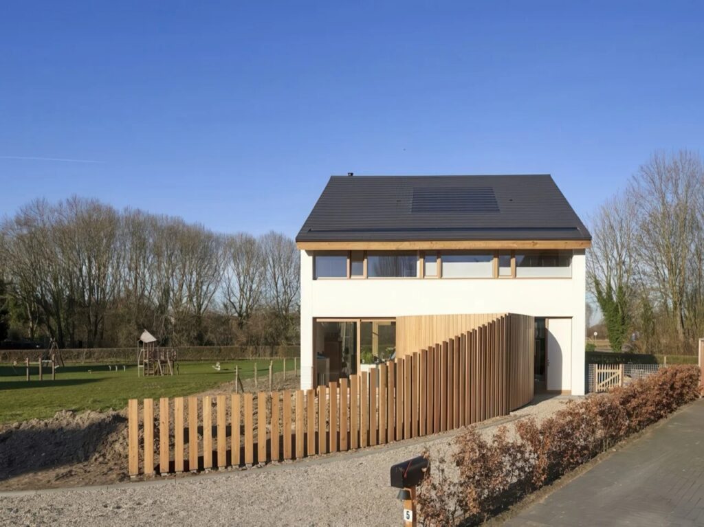 Street-level view of a modern barnhouse with white horizontal wood cladding and a curved timber fence.