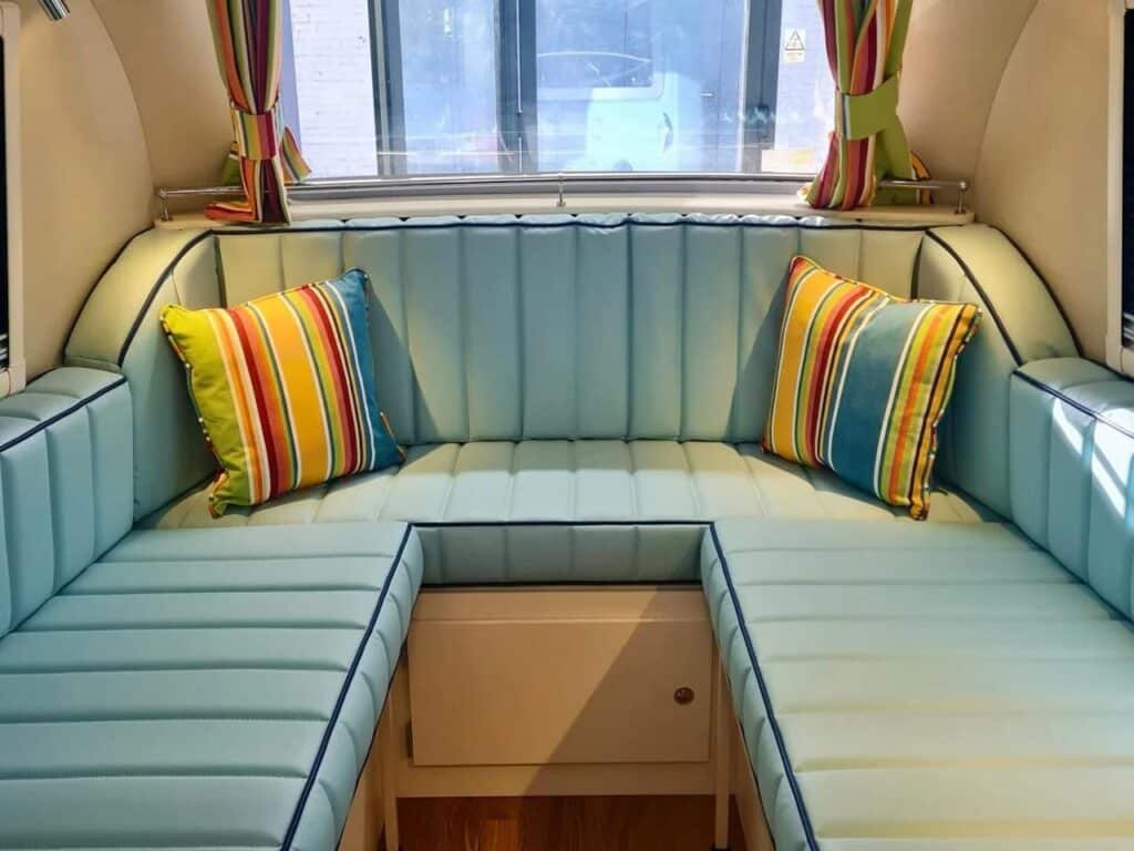 Interior view of the Barefoot Bothy showing a U-shaped light blue seating area with colorful striped pillows.