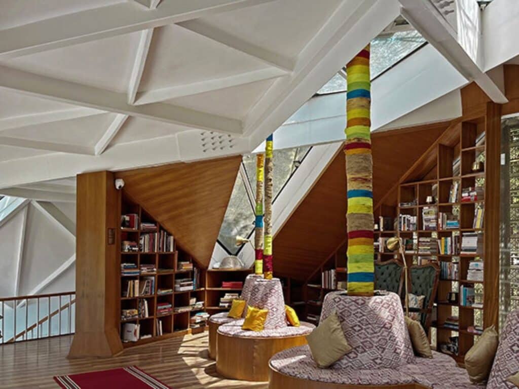 A communal library area with circular seating and vibrant textile-wrapped pillars under a white faceted ceiling.