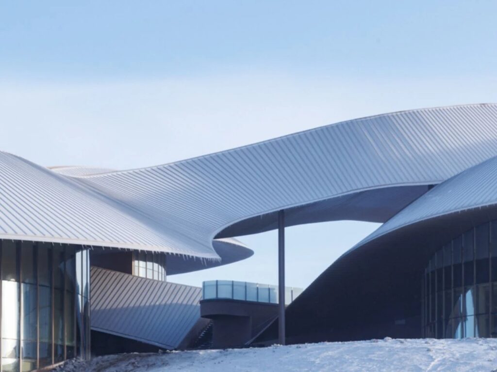 Detailed architectural view of the interlocking roof layers and a staircase at the Volcano Visitor Center against a clear blue sky.