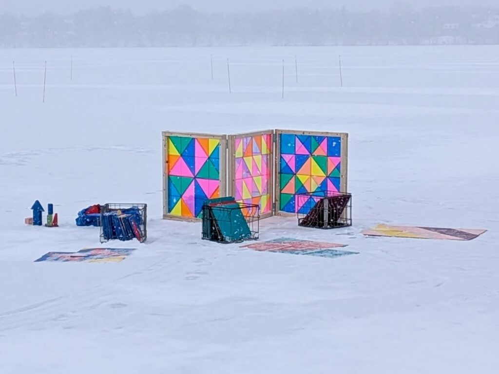 An outdoor interactive puzzle station on ice featuring colorful geometric triangular patterns in wooden frames.
